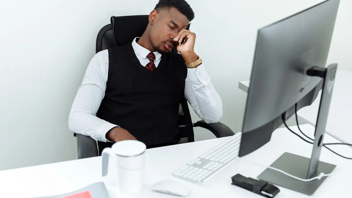 A man in business attire resting his head at an office desk, displaying workplace fatigue.