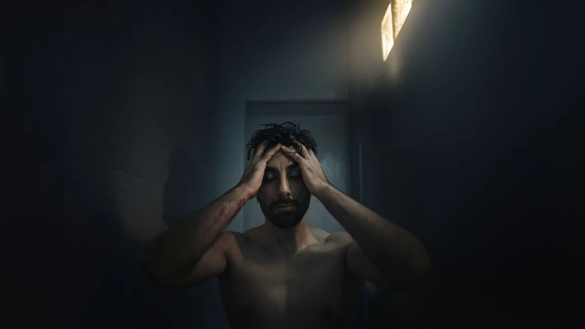 A man in a dimly lit room holds his head in thought, portraying deep emotion and introspection.