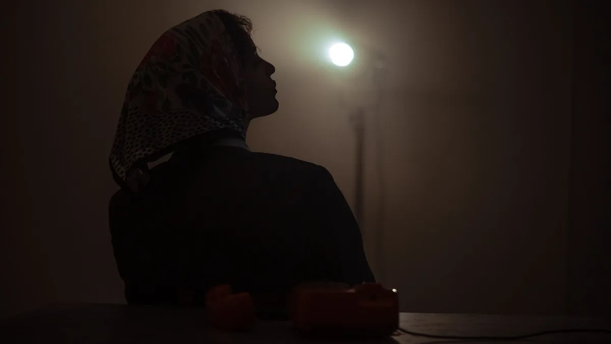 Silhouette of a woman wearing a headscarf in a dark room, facing a light source.