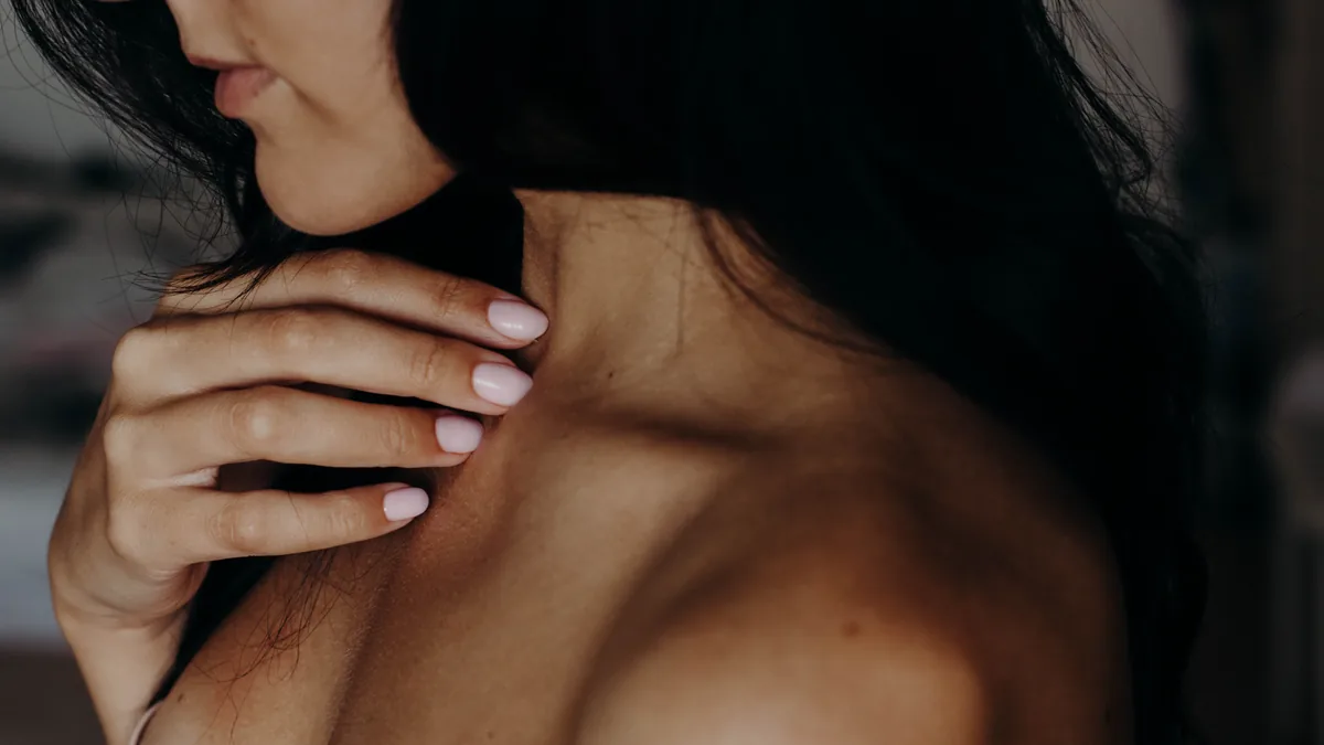 Intimate close-up of a young woman's neck, shoulder, and hand with a gentle touch.