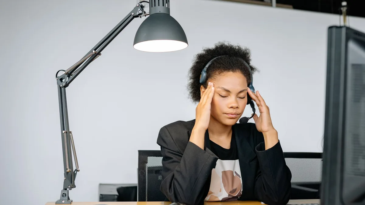 Exhausted call center agent with headset, tired from work, in an indoor office setting.
