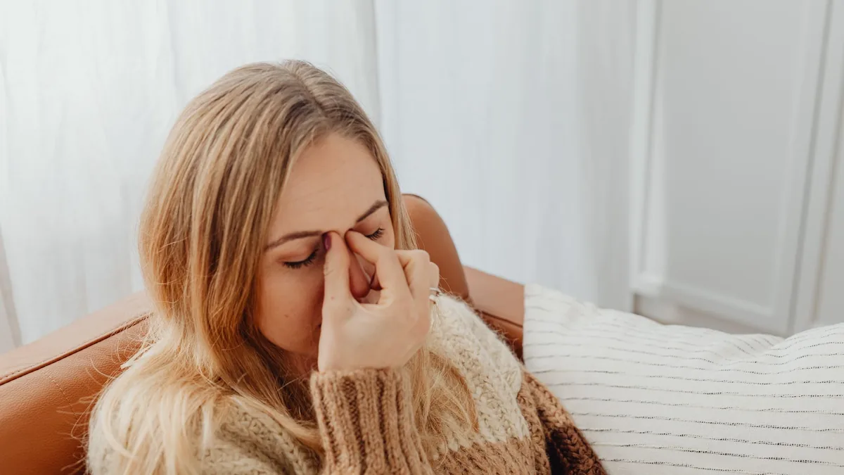 A woman sitting on a couch with eyes closed, holding her nose in apparent sinus pain.