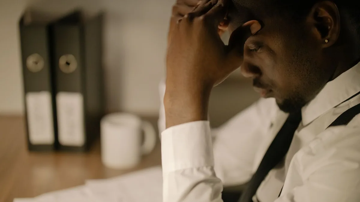 Side view of a stressed businessman in white shirt holding head at a desk with papers.
