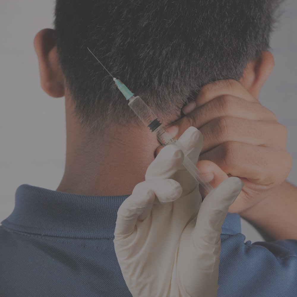 A gloved clinician positions a syringe at the base of a patient's skull to perform an occipital nerve block.