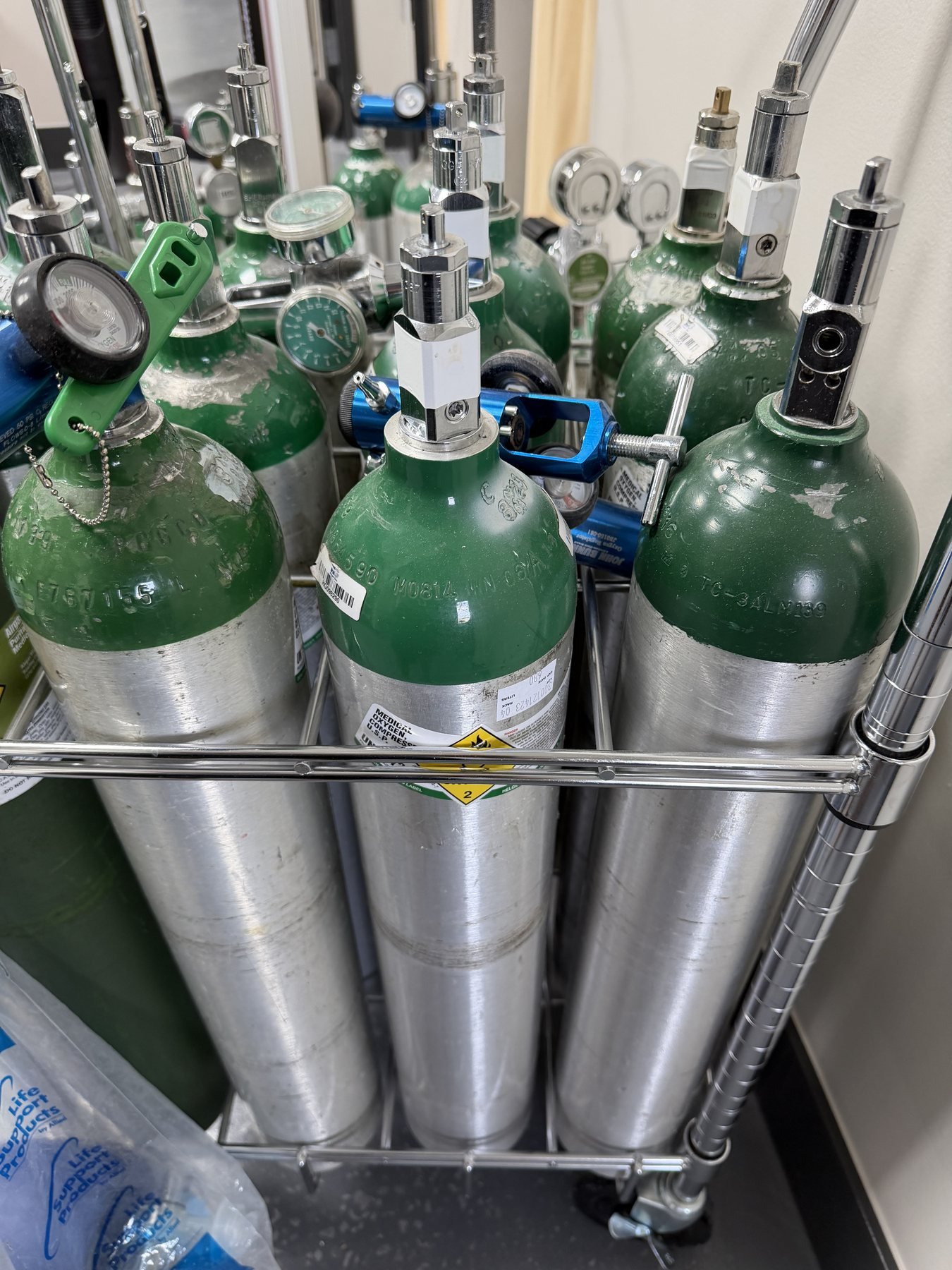 Medical oxygen cylinders with flowmeters and regulators alongside a non-rebreather mask set, the delivery used for high-flow oxygen in cluster headache