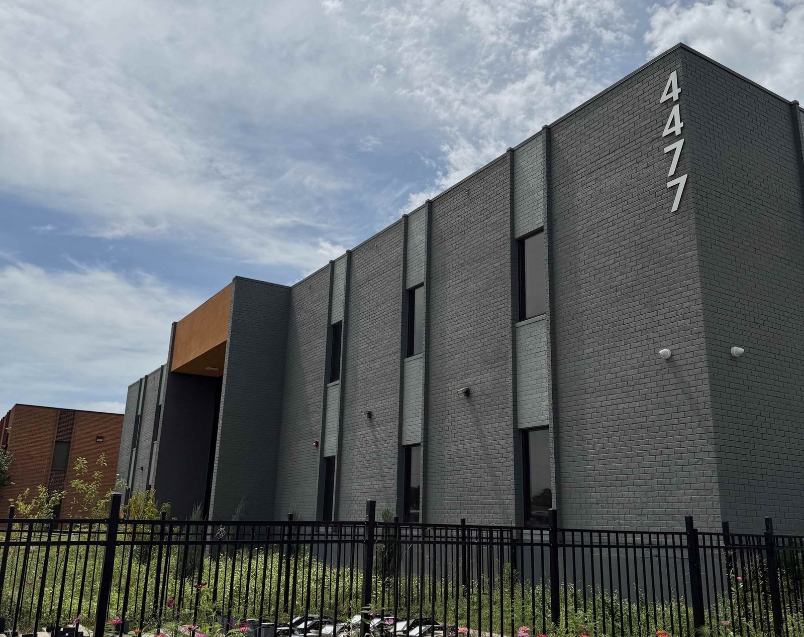 Wide view of the 4477 Woodson Road building in St. Louis, with the building number on the corner, the orange entrance canopy and the planted frontage