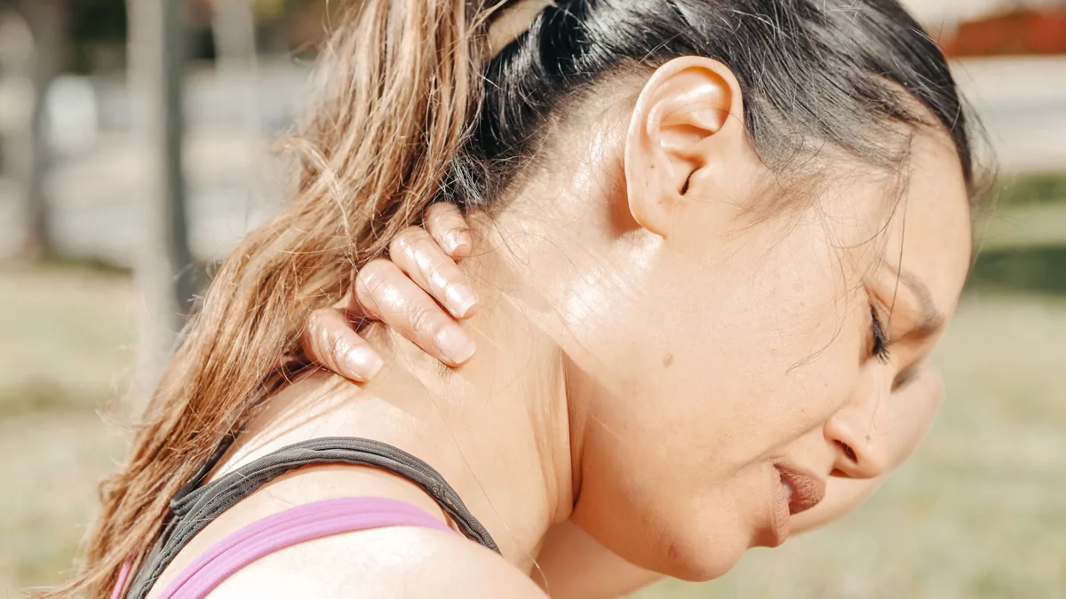 A woman holds the side of her neck as pain spreads up toward her head