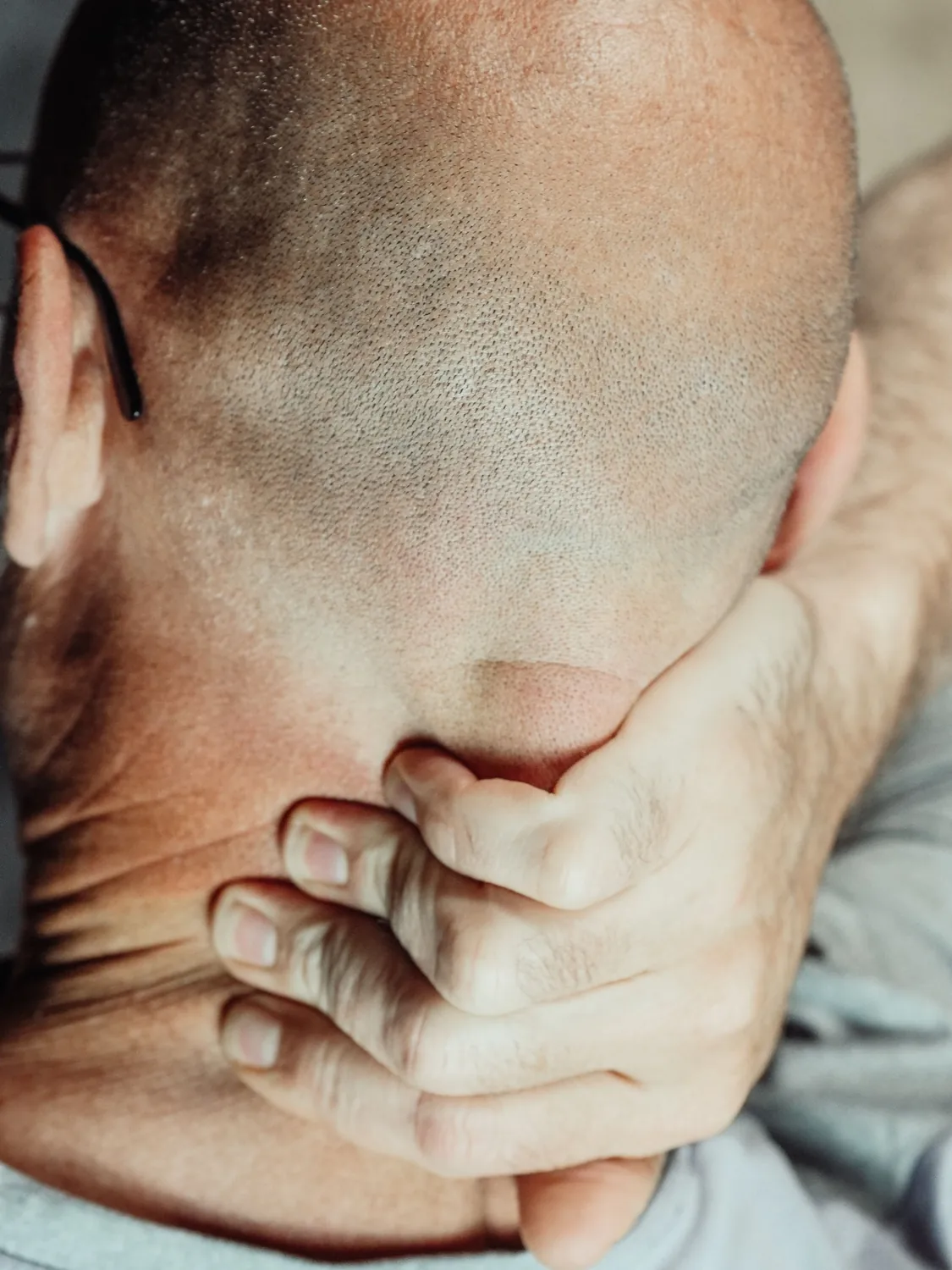 Man with head bowed holding the back of his neck, where a cervicogenic headache can start
