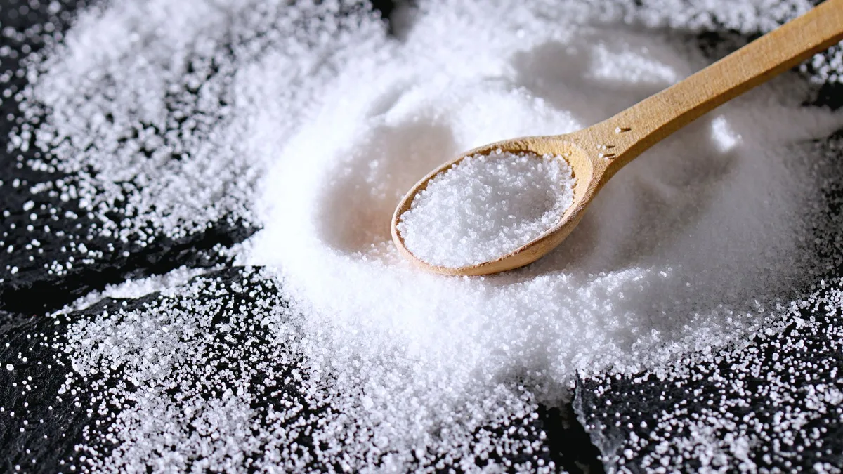 A wooden spoon resting in a pile of fine white salt on a dark slate surface
