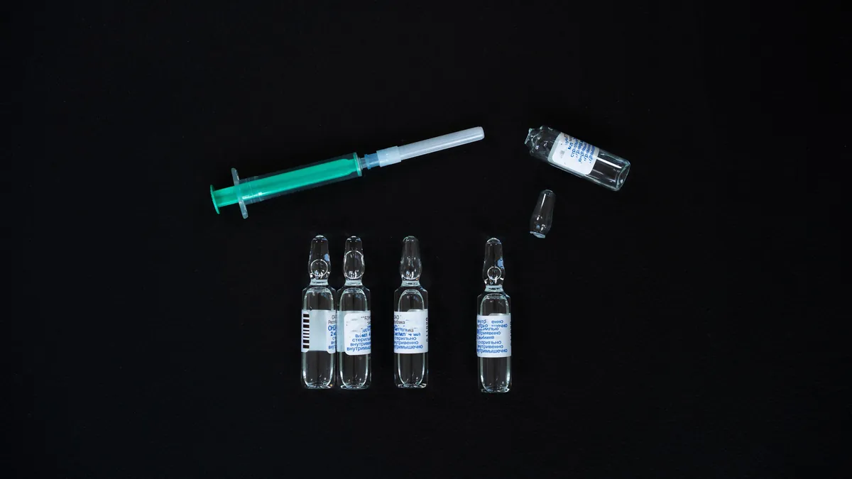 Glass medication ampoules and a syringe on a dark surface