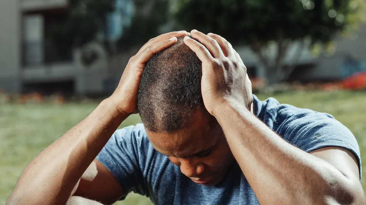 A man with his head bowed presses both hands to the back of his head, where occipital nerve pain is felt